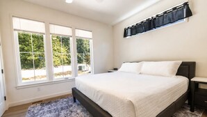 Un dormitorio con una cama grande, una mesita de noche, un estante en la pared y un ventanal con persianas.