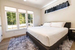 Une chambre avec un grand lit, une table de chevet, une étagère fixée au mur et une fenêtre avec des stores.