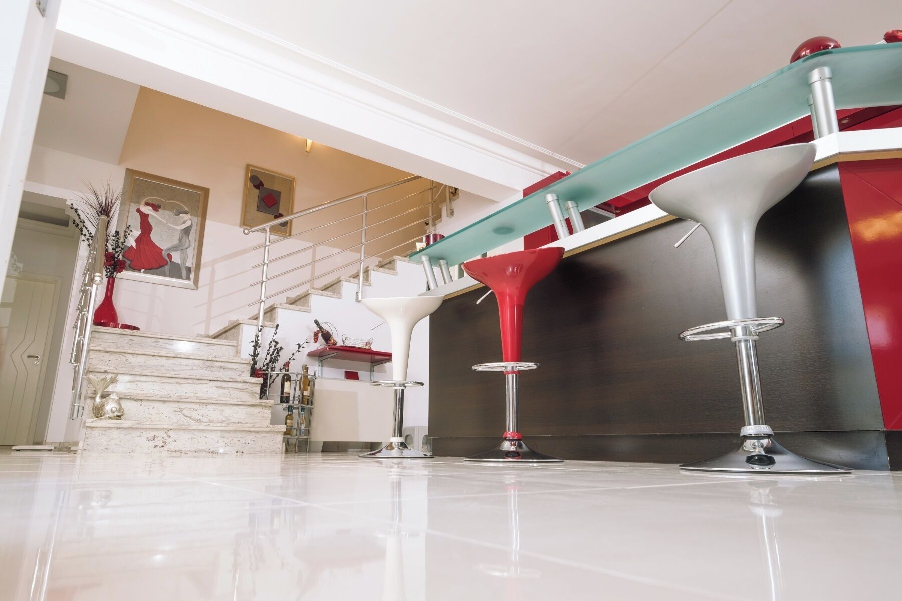 A modern interior with a staircase, a glass railing, and a red and white bar area.
