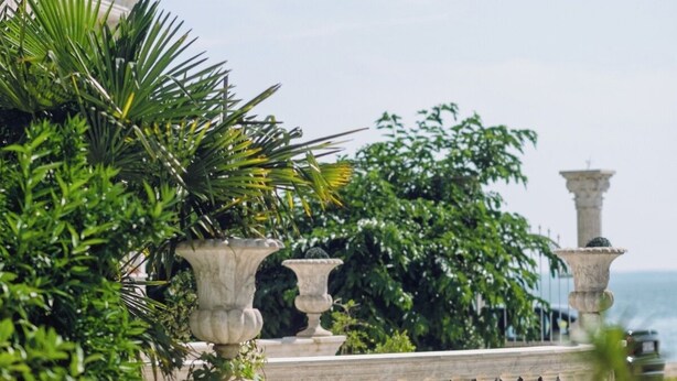 Een balkon met een balustrade, plantenpotten en uitzicht op zee.