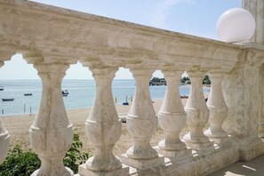 Een stenen balustrade met uitzicht op een strand, met boten en een pier in de verte.
