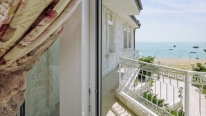 Een balkon met uitzicht op zee en strand, een witte balustrade en een gevel.