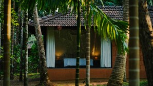 A single-story building with a tiled roof, surrounded by dense tropical foliage. - Arika Goa (Neturlim)