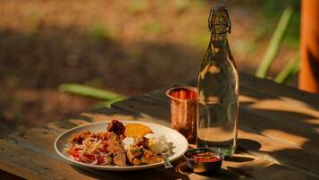 Una mesa de picnic de madera con un plato de comida, una botella y una taza metálica pequeña.
