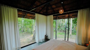 A bedroom with a large bed, white curtains, and a view of a forest. - Arika Goa (Neturlim)