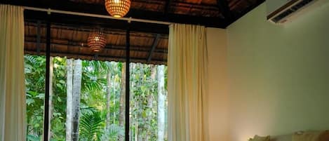 A room with a bed, curtains, and a view of greenery outside.
