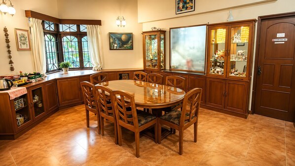 A dining area with a round table, wooden chairs, and a kitchen area with cabinets and a refrigerator. - Arika Goa (Neturlim)