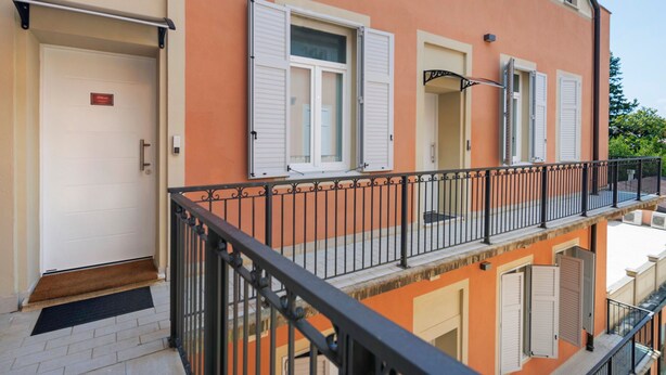 Ein mehrstöckiges Gebäude mit Balkon, einer Tür mit Fußmatte und einem Fenster mit Rollläden.