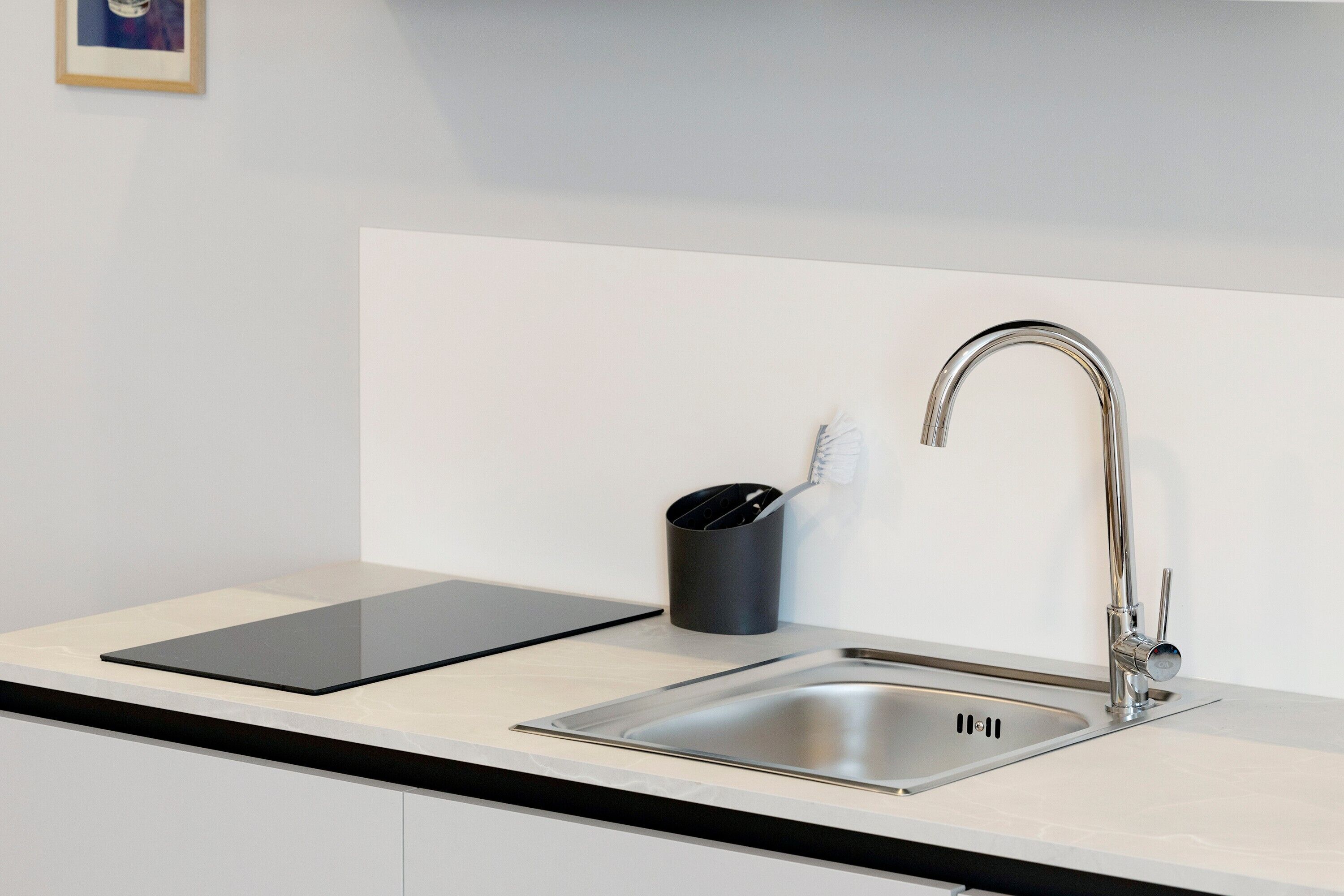 A modern kitchen with a stainless steel sink, a black tablet on the counter, and a black cup with utensils.