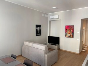 A modern living room with a grey sofa, a flat-screen TV, an air conditioning unit, and two artworks on the walls. - Apartment 'Verdi' in Gorizia (Gorizia)