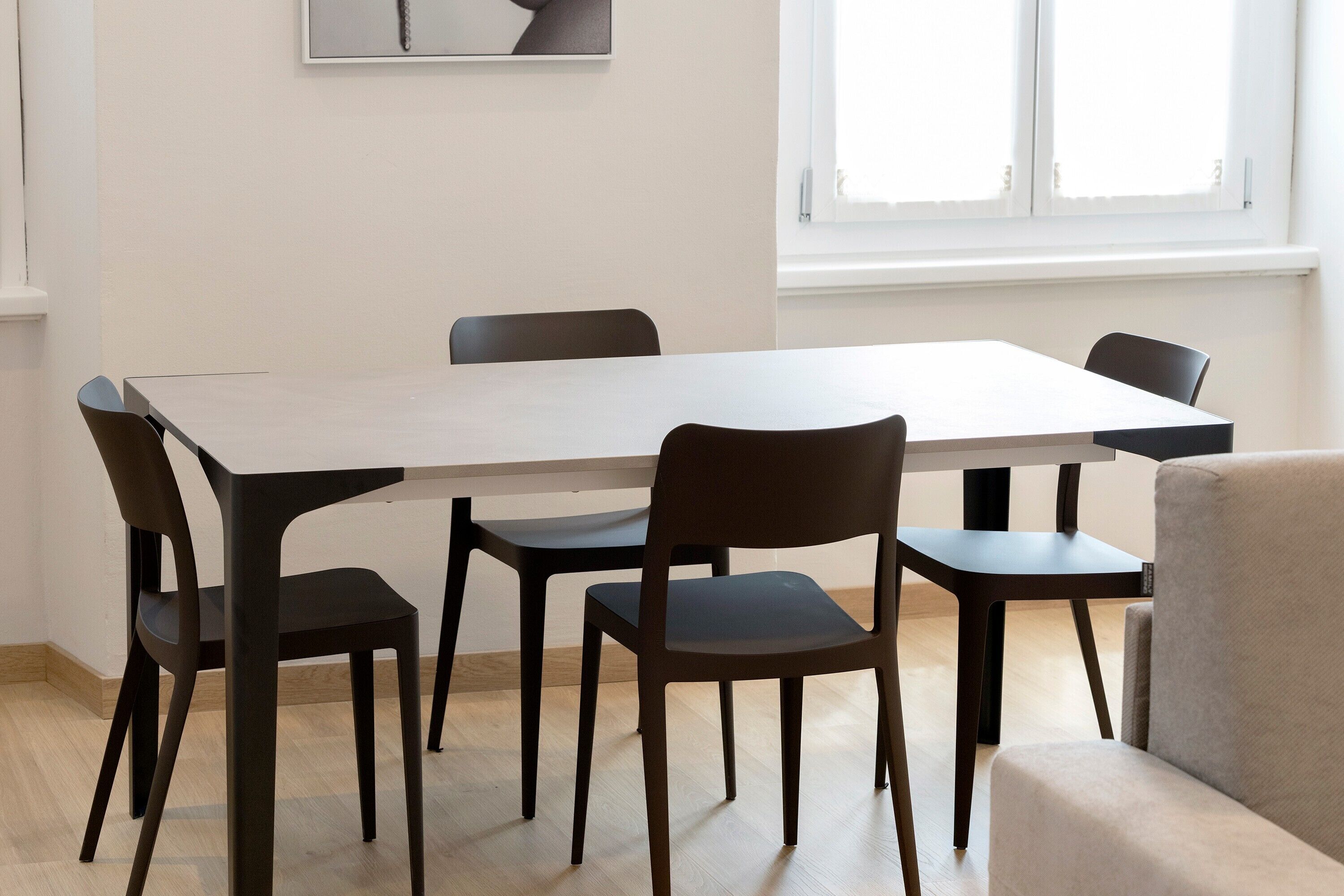 Een eetruimte met een rechthoekige tafel, zes stoelen en een raam met zonwering.