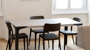Een eetruimte met een rechthoekige tafel, zes stoelen en een raam met zonwering.