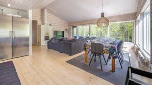 Une cuisine moderne avec un réfrigérateur en acier inoxydable, un coin repas avec une table dressée pour quatre personnes et un grand canapé gris.