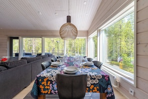 En matplats med ett bord dukat för sex personer, stora fönster, ett tak med träribbor och en soffa i bakgrunden.