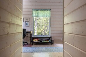 Una habitación con paredes de madera, un escritorio, una silla, una ventana con vistas a árboles y una estantería.