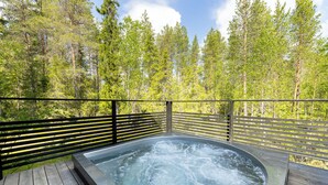 Un bain à remous entouré d’une terrasse en bois, avec une forêt en arrière-plan.