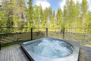 Ett bubbelbad omgivet av ett trädäck med en skog i bakgrunden.