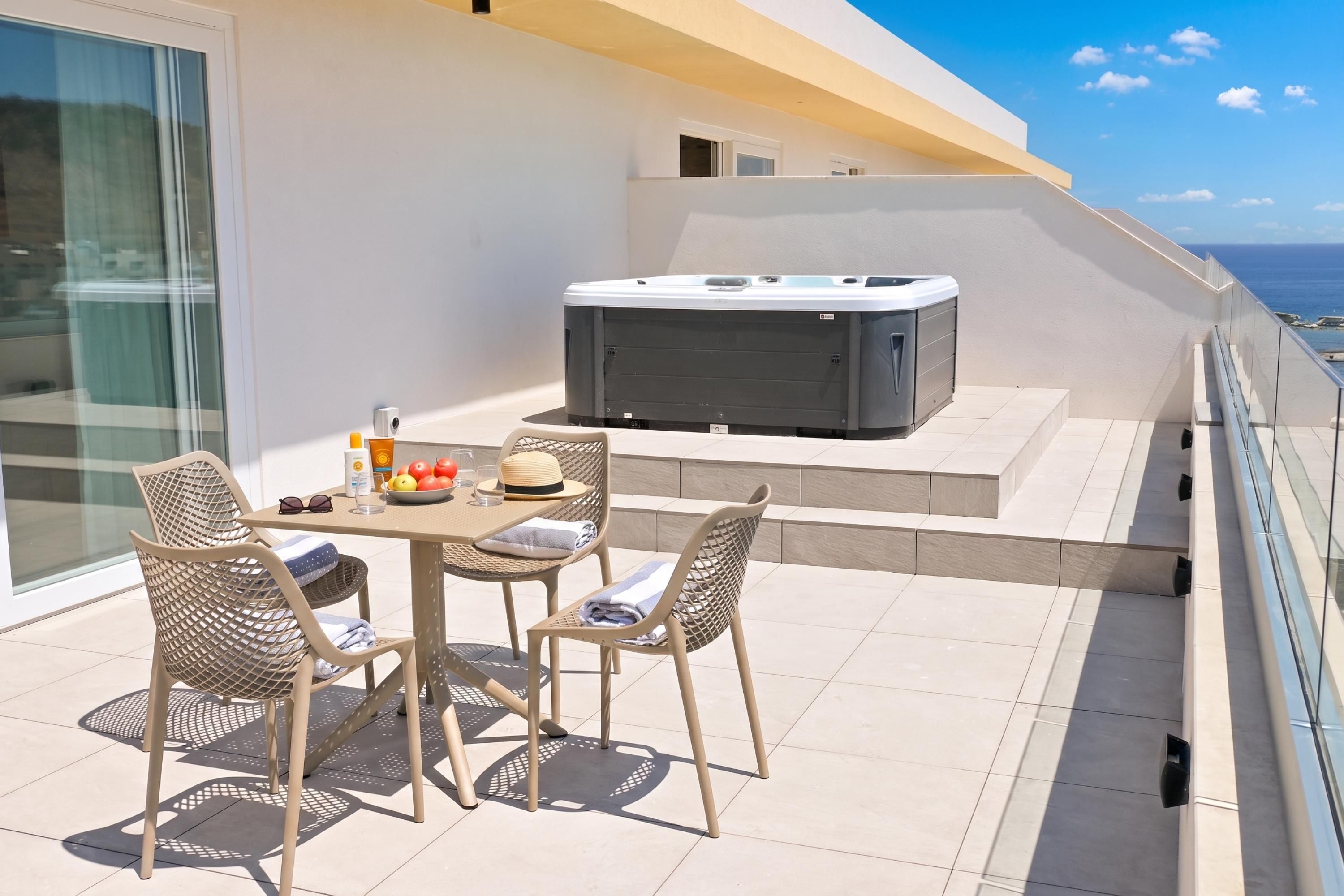 Een balkon met een tafel en stoelen, een jacuzzi en uitzicht op zee.