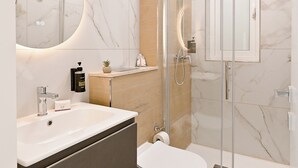 A modern bathroom with a glass shower enclosure, a white sink, and a marble-tiled wall. - Modern Seaside Apartments (Zebbug)