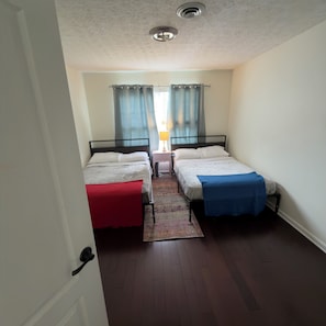 Een kamer met twee bedden, een nachtkastje, een lamp en een raam met gordijnen.