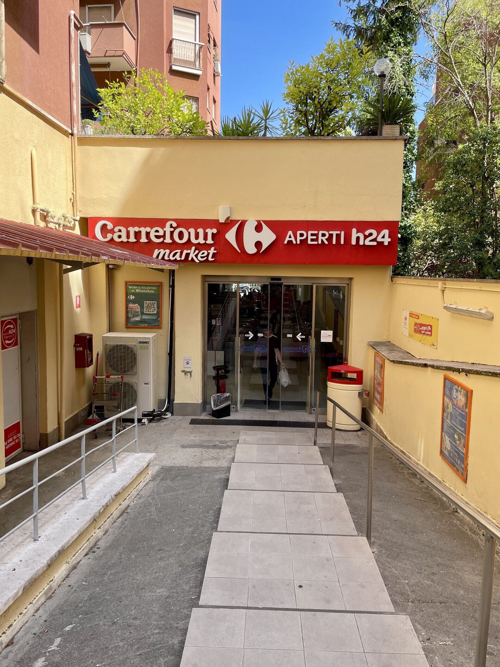 Ein Carrefour-Markt mit gut sichtbarem Eingang, einer Rampe, die zur Tür führt, und einem Automaten in der Nähe.