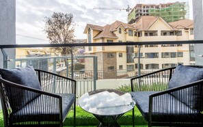Ein Balkon mit zwei Stühlen und einem Tisch, der auf einen Wohnbereich mit Gebäuden und einer Baustelle blickt.