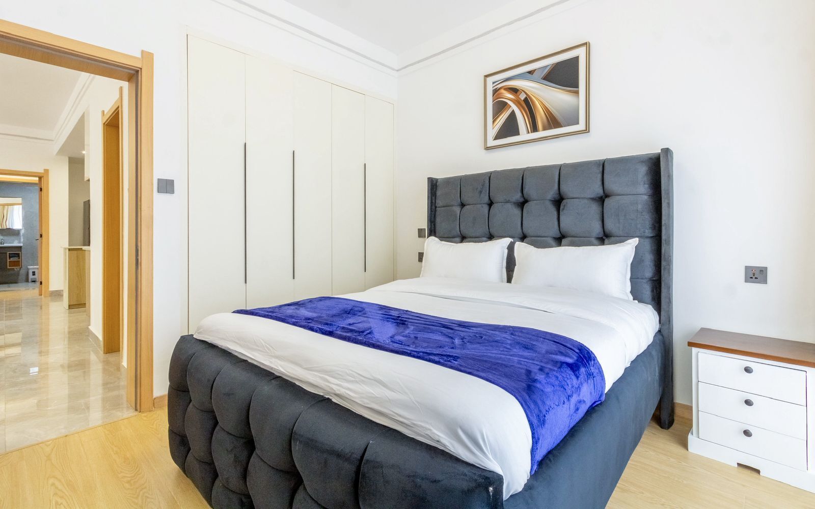 A bedroom with a large bed, a nightstand, a wardrobe, and a painting on the wall.