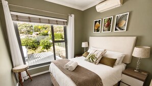 A hotel room with a bed, bedside tables, a window with curtains, and a view of greenery outside. - Villa Atlantica  (Cape Town)