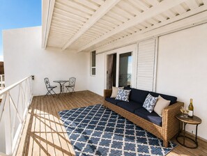 Een balkon met een rieten bank, een klein tafeltje met glazen en een kamerkleed met dessin.