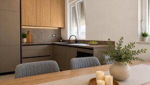 A modern kitchen with a wooden countertop, a sink, and a window with blinds. There is a dining table with chairs and a vase with a plant. - Amazing home in Privlaka (Privlaka)
