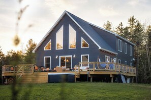 A large house with a deck, multiple windows, and a staircase leading to a second level. - NEW - Acadia Retreat - Hot Tub, Deck, Games - Sleeps 14 (Tremont)