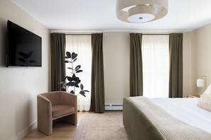 Ein modernes Hotelzimmer mit Bett, Sofa, Fernseher und einem großen Fenster mit Vorhängen.