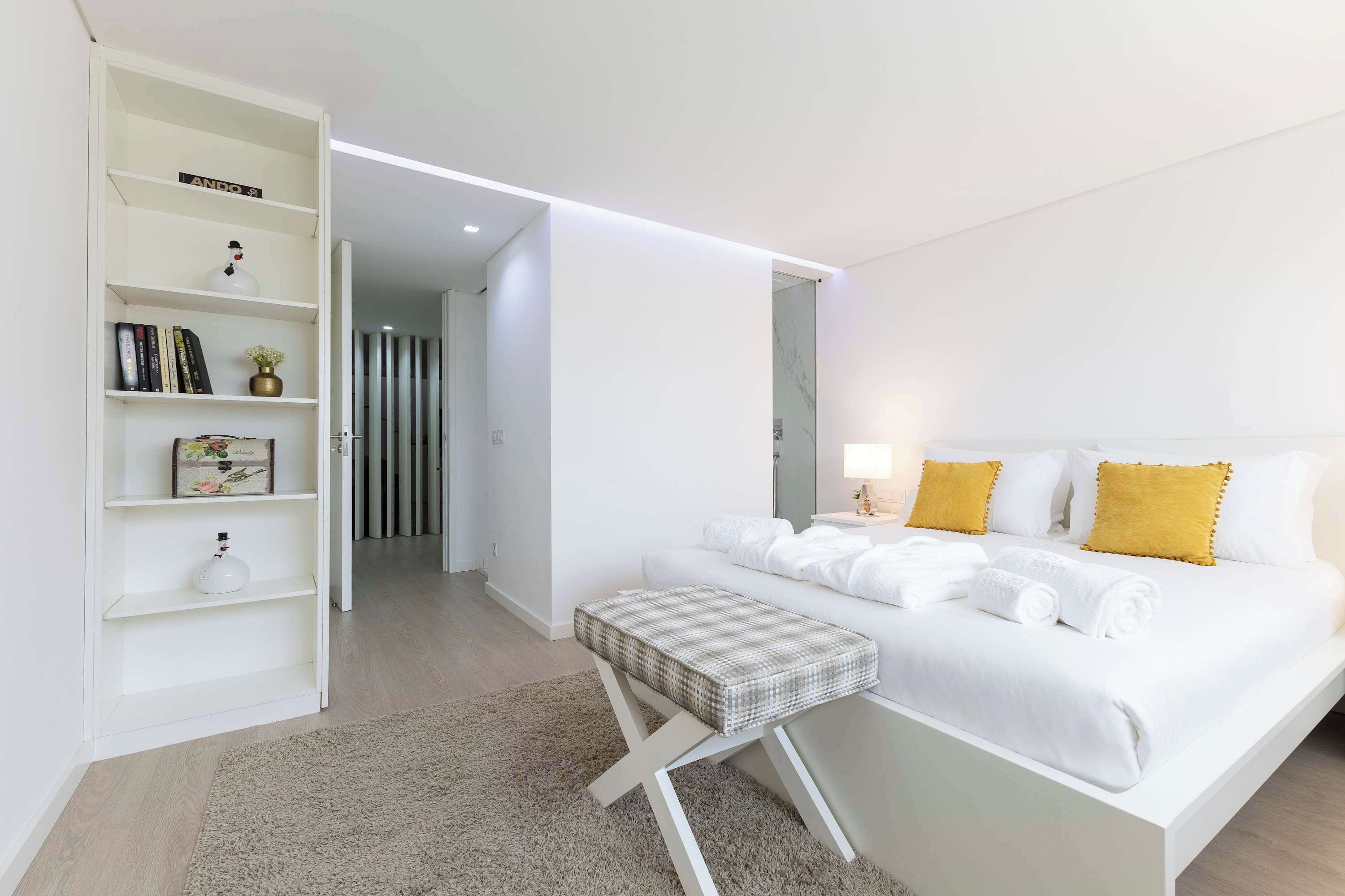 Quarto de hotel moderno com cama, mesa de cabeceira e uma estante branca.