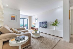 Een moderne woonkamer met een bank, salontafel, televisie en kunstwerk.