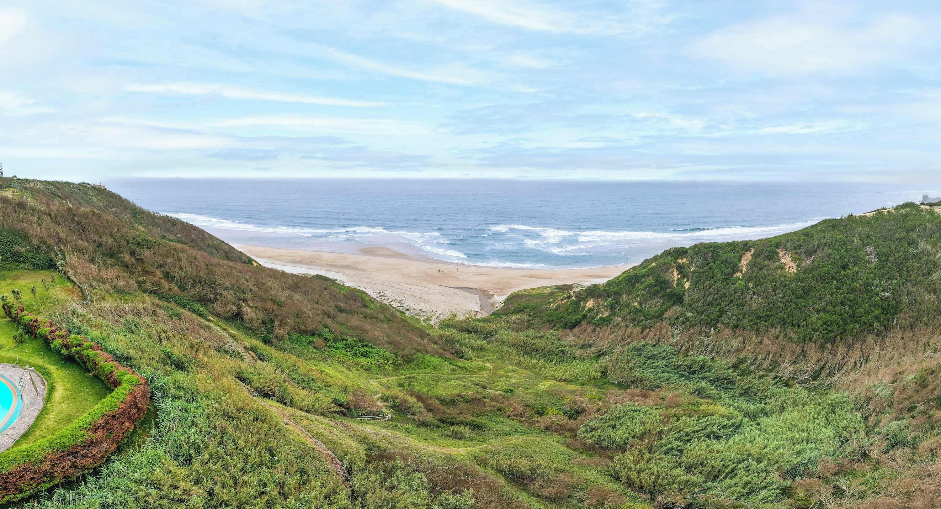 A coastal landscape with a beach, rolling hills, and a clear sky.