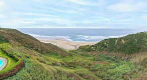 Een kustlandschap met een strand, glooiende heuvels en een heldere lucht.