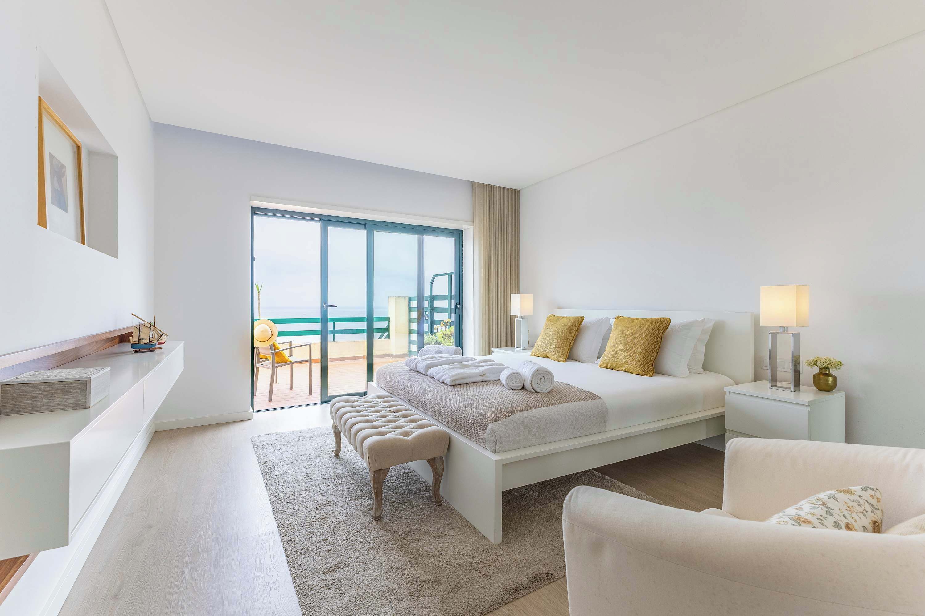 Une chambre d’hôtel moderne avec un grand lit, un coin salon comprenant un fauteuil et une petite table, ainsi qu’un balcon avec vue.