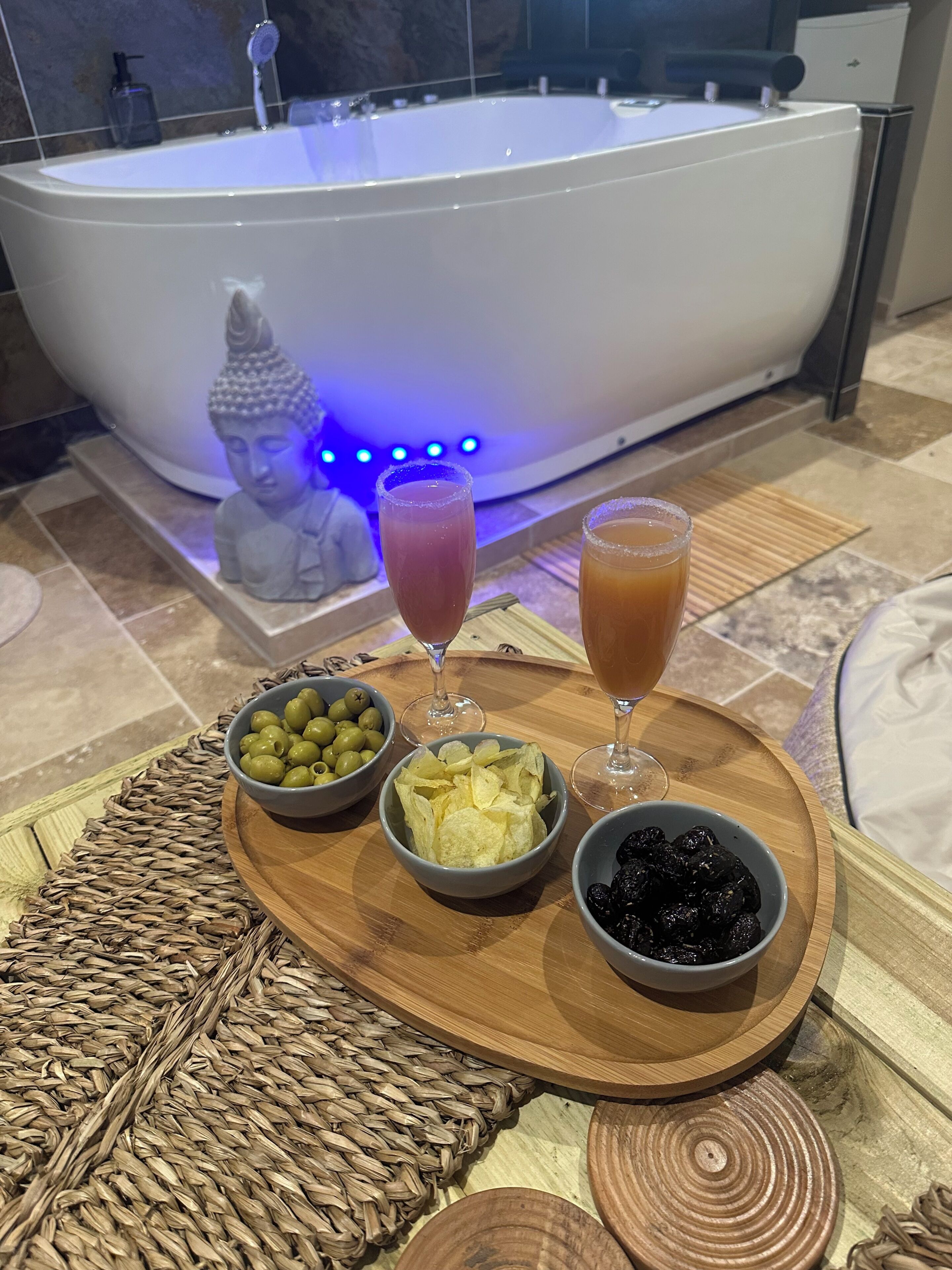 Un espace bien-être comprenant une baignoire, une statue de Bouddha et un plateau avec des collations et des boissons.