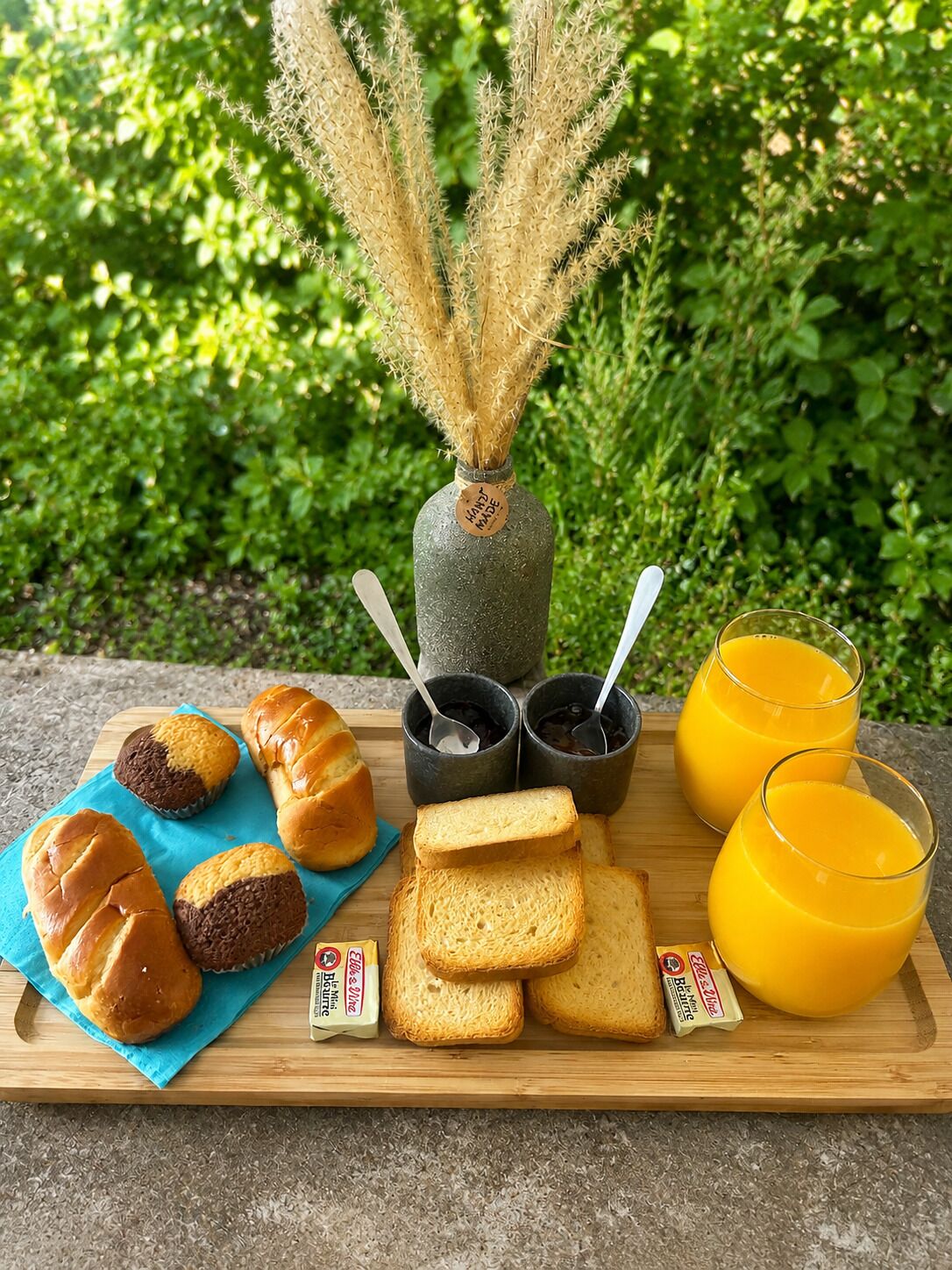 A breakfast tray with bread, pastries, jam, and orange juice on a wooden board.