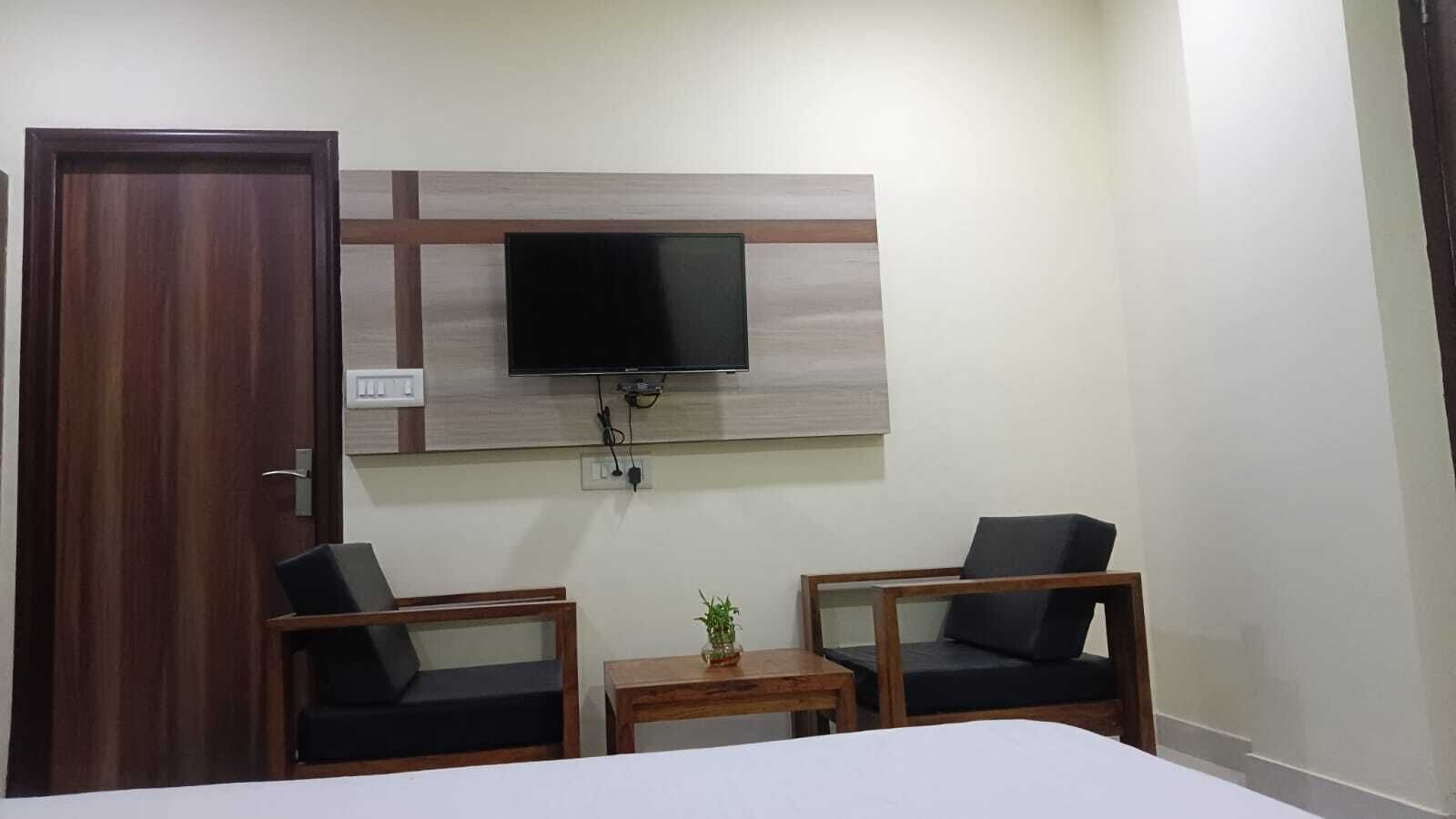 Una habitación de hotel con una cama, dos sillones, una mesita con una planta, un televisor montado en la pared y una puerta de madera.
