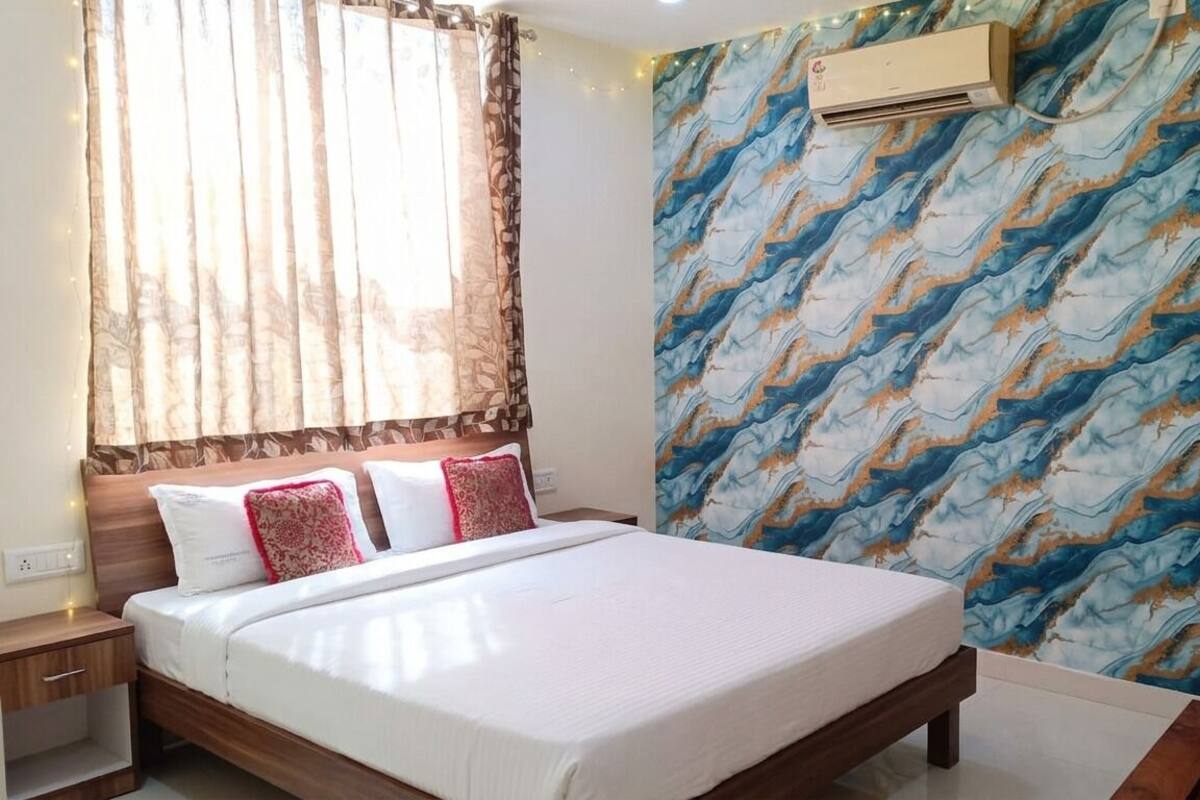 A bedroom with a bed, curtains, an air conditioning unit, and a patterned wall.