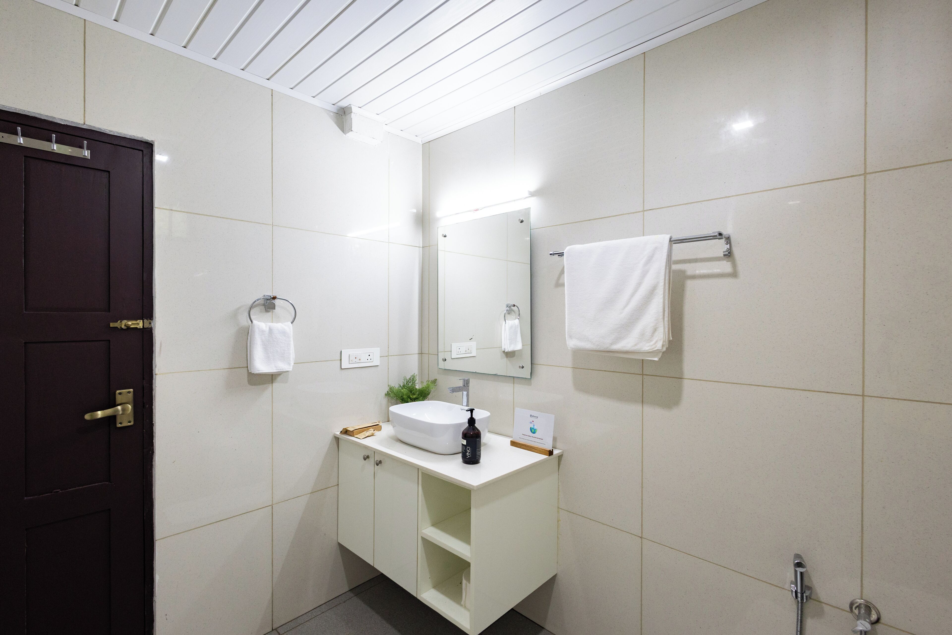 A modern bathroom with a dark door, white tiles, a sink with a mirror, and a towel rack.