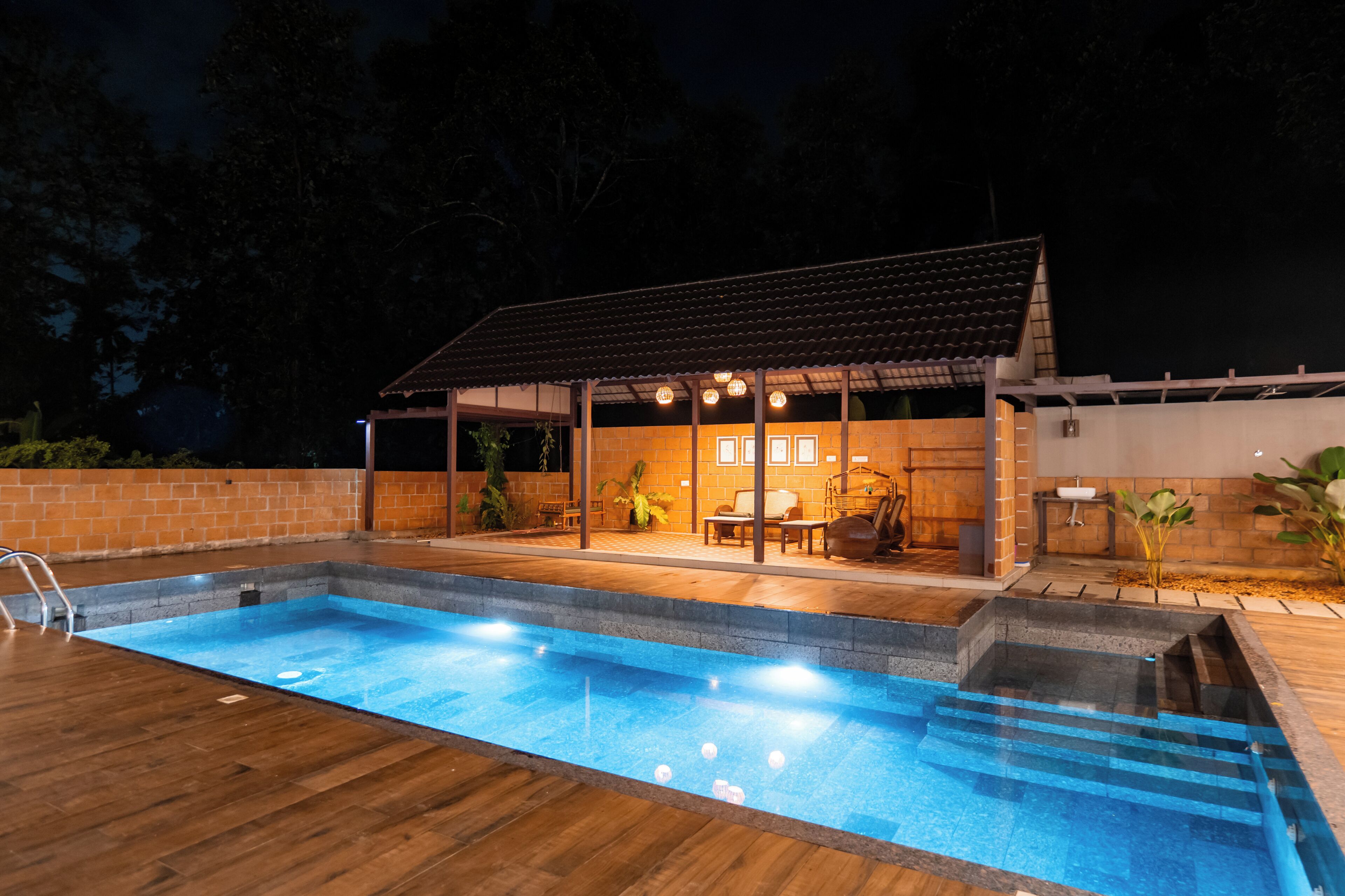 Una piscina con muelle de madera, un patio cubierto con asientos y una pared de ladrillo.