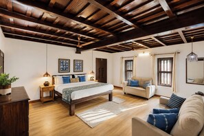 Une chambre avec un plafond en bois, un lit recouvert d’une couvre-lit à motifs, un canapé et une fenêtre avec des rideaux.