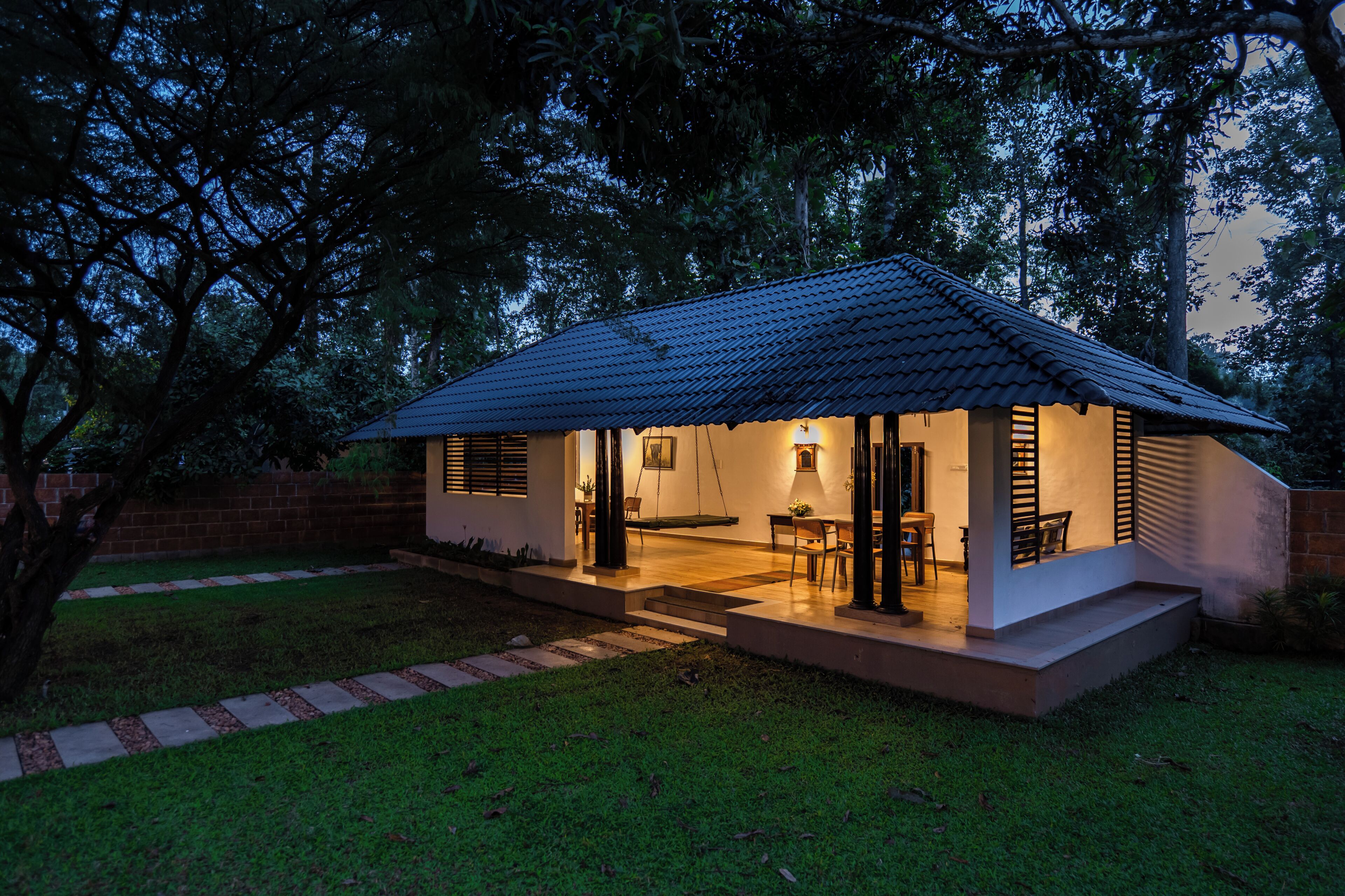 A small house with a tiled roof, a porch with chairs, and a well-maintained lawn.