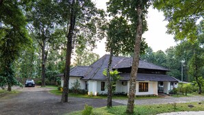 Uma casa com telhado de telhas, cercada por árvores e uma entrada por meio de um caminho.