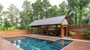 Piscina com deck de madeira, área de estar coberta e muro de tijolos.