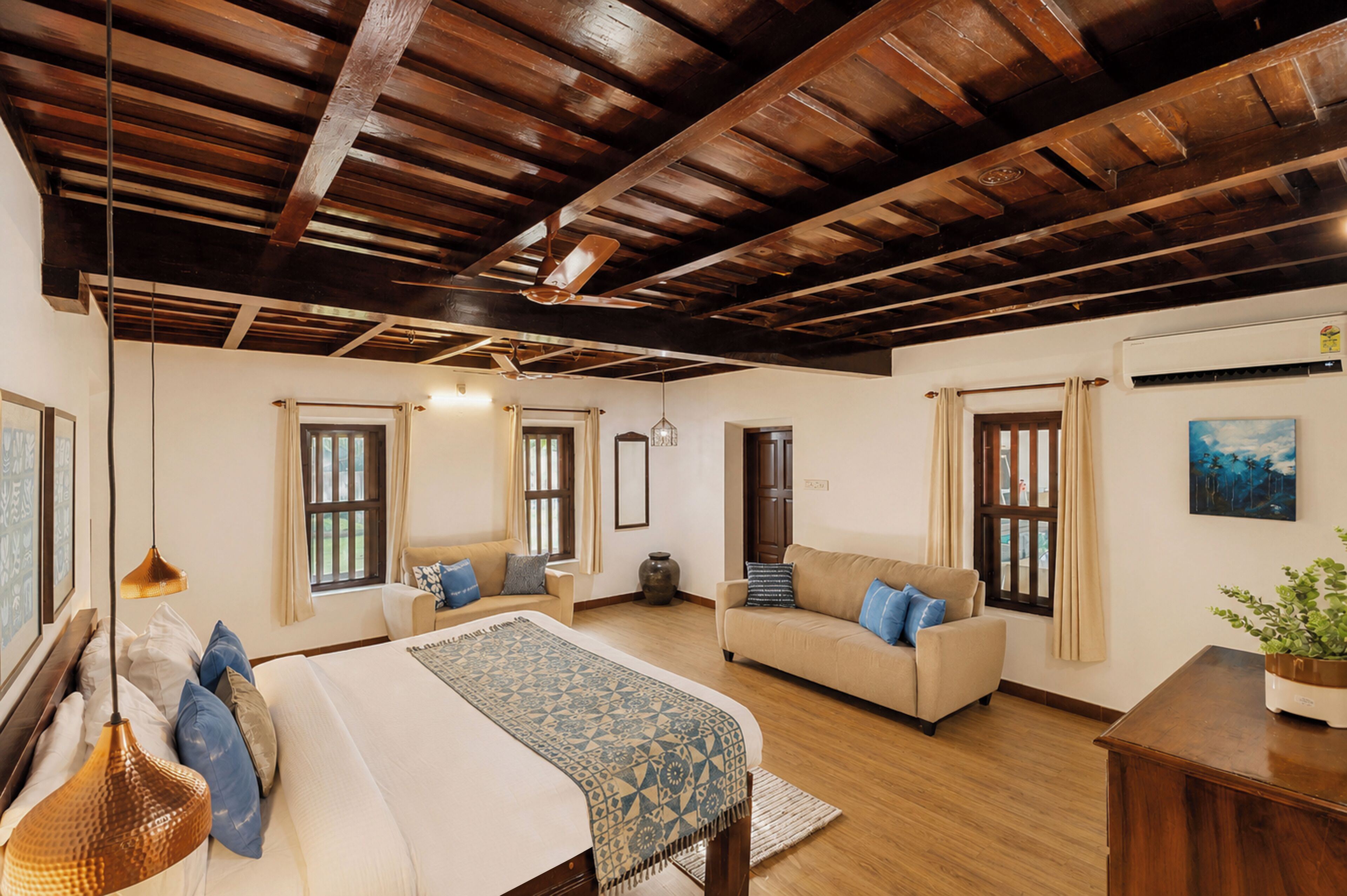 Una habitación amplia con una cama grande, un sofá, techo de madera y una ventana con cortinas.