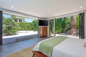 Ein Schlafzimmer mit Bett, Fernseher und Blick auf einen Garten.