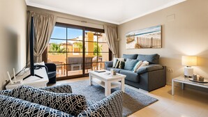 Uma sala de estar moderna com um sofá, uma mesa de centro, uma luminária e vista para o exterior através de grandes janelas.
